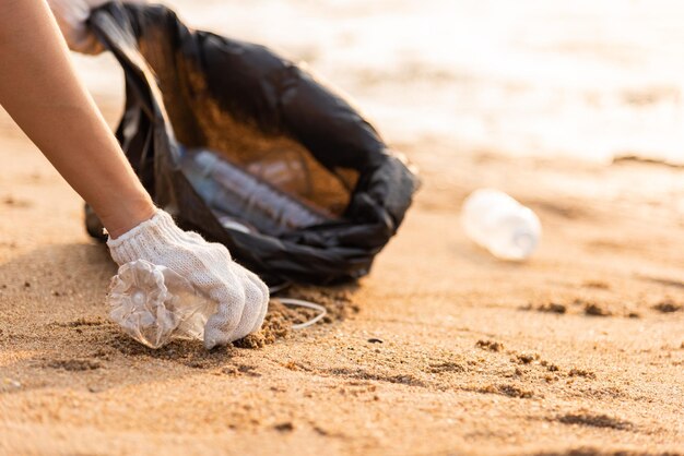 Mulher voluntária pegando garrafa de plástico em saco plástico de lixo preto para limpar a praia