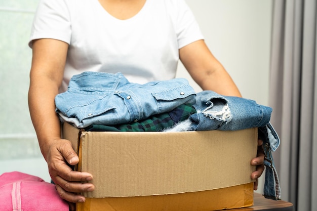 Mulher voluntária segurando caixa de doação de roupas com roupas usadas em casa para apoiar a ajuda aos pobres do mundo