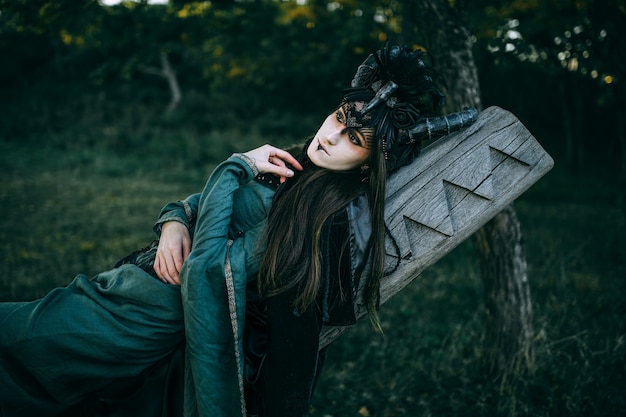 Mulher-xamã com chifres em vestido verde andando na floresta