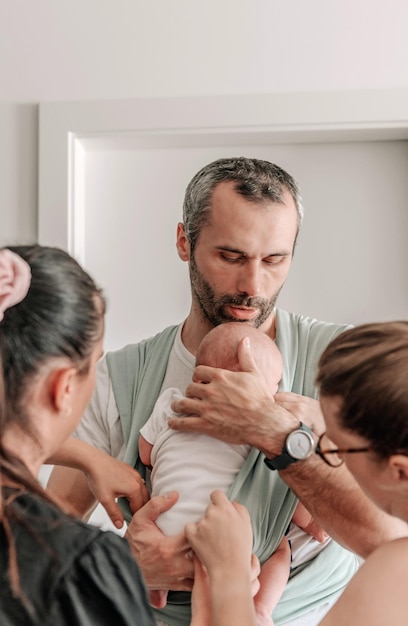 Mulheres a ajudar o pai a embrulhar o bebé num fio de bebé