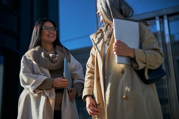 Mulheres alegres com laptops paradas na rua