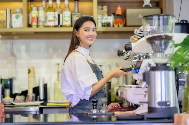 Mulheres asiáticas Barista sorrindo e usando a máquina de café no balcão da cafeteria