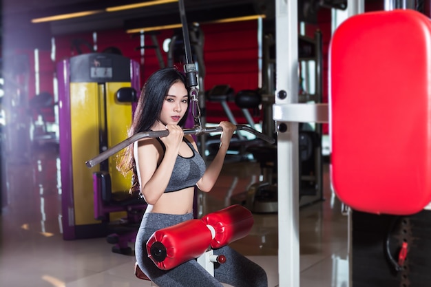 Mulheres asiáticas da aptidão que executam fazendo os exercícios que treinam os músculos do ombro e da caixa no interior e no health club do gym do esporte.