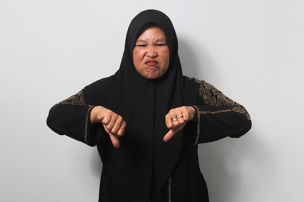 Mulheres asiáticas de meia-idade chateadas usando hijab mostram o polegar para baixo e dão opinião negativa