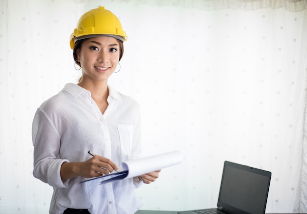 Mulheres asiáticas engenharia de inspeção e trabalho e segurando plantas no escritório