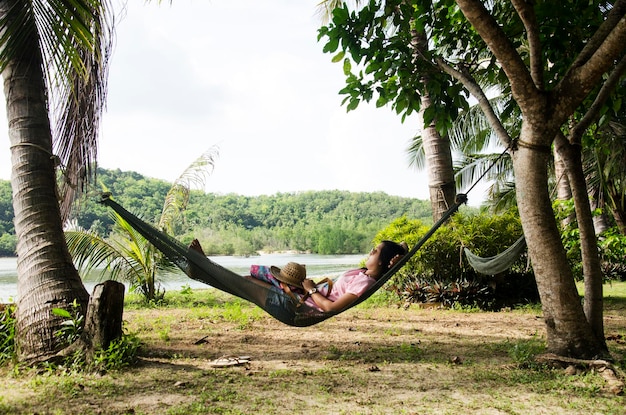 Mulheres asiáticas sentam e relaxam em móveis Rede pendurada entre palmeiras no jardim do resort em frente à praia e água do mar tropical em Ko Yao Noi em Phang Nga Tailândia
