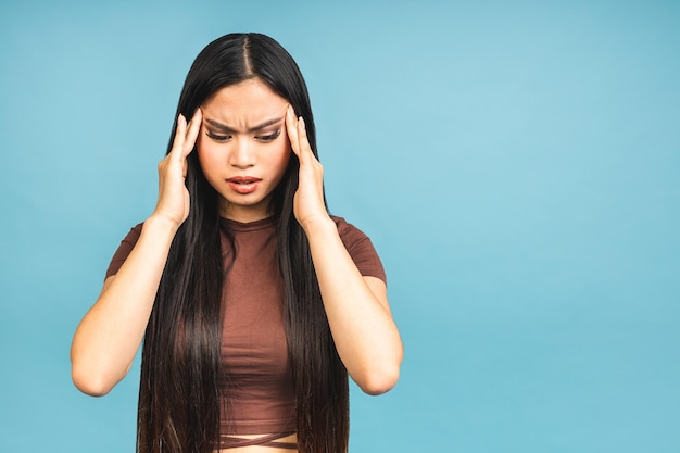 Mulheres bonitas asiáticas se sentindo confusas e com dor de cabeça isoladas sobre fundo de cor azul Conceito de trabalho duro sem manter a saúde e o estresse no ambiente atual