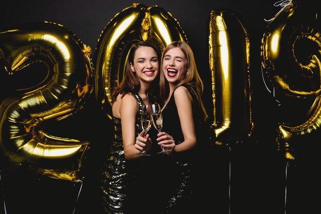 Mulheres bonitas comemorando o ano novo. Garotas lindas e felizes em vestidos de festa sensuais elegantes segurando balões de ouro de 2019, se divertindo na festa de ano novo. Celebração do feriado. Imagem de alta qualidade