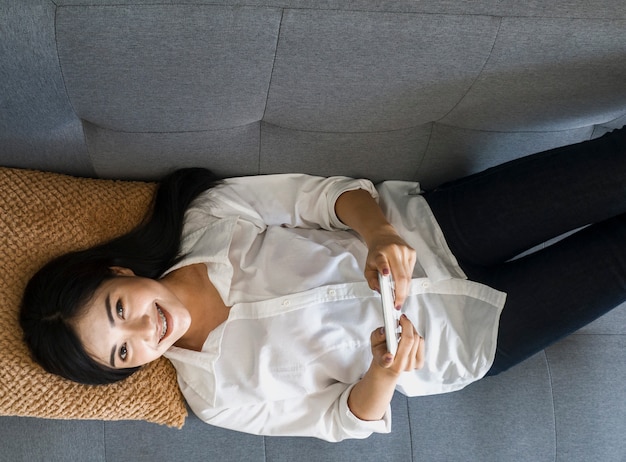 Mulheres bonitas em vestidos brancos usam telefones móveis on-line no sofá. conceito de compras on-line