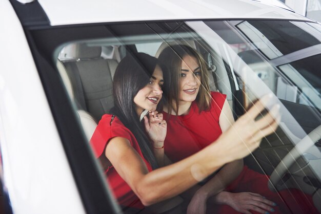 Mulheres bonitas gêmeas sentado nos bancos da frente e sorrindo enquanto posava