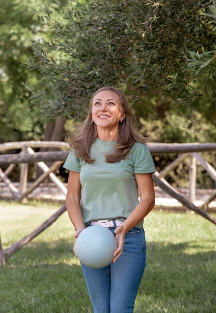 Mulheres brancas de meia idade vestindo camiseta e jeans brincam com uma bola no parque, três quartos de tiro