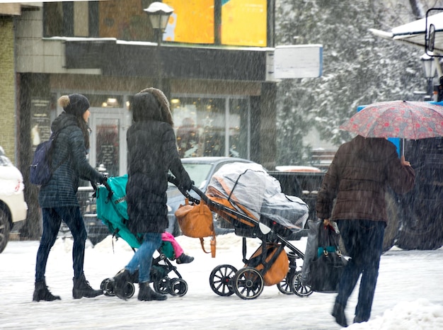 Mulheres com filhos pequenos nos carrinhos, andando pela rua. Dia de inverno com neve. Desfoque de movimento intencional. Imagem desfocada