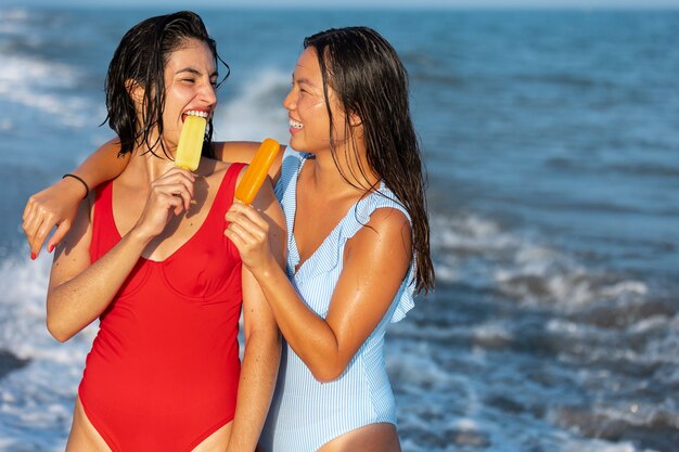 Foto mulheres com sorvete no plano médio à beira-mar