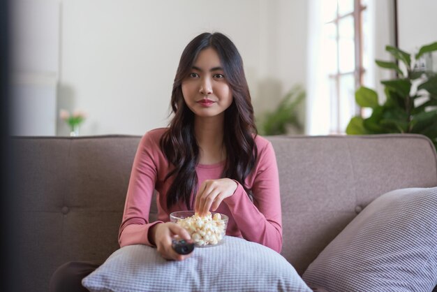 Mulheres comem pipoca e trocam de canal com controle remoto enquanto assistem TV no estilo de vida em casa