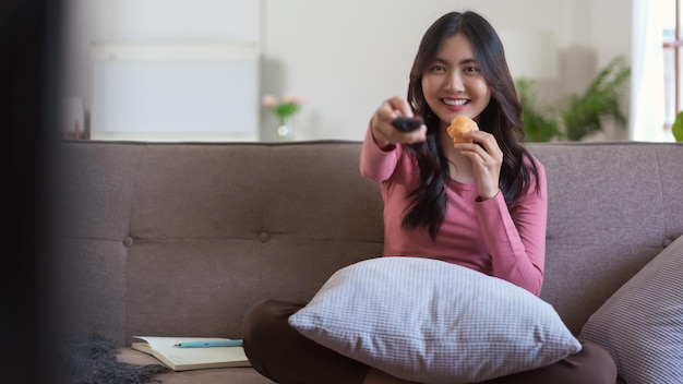 Mulheres comendo pão e escolhendo canal com controle remoto enquanto assistem TV no estilo de vida em casa