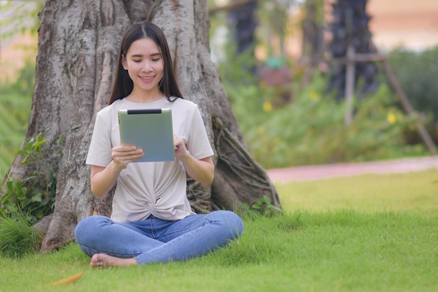 Mulheres de beleza usando tablet lendo E-book sentado na manhã de parque da cidade fresca