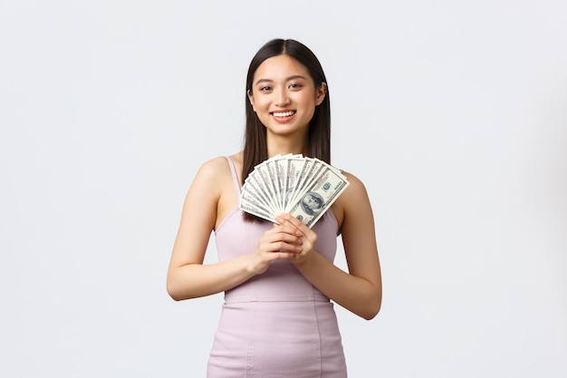 Mulheres de luxo, conceito de festa e feriados. Linda mulher sorridente asiática em vestido de noite, mostrando dinheiro