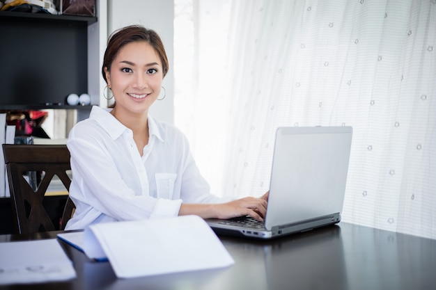 Mulheres de negócios asiáticas bonitas, verificando o documento e usando o notebook e sorrindo feliz por trabalhar