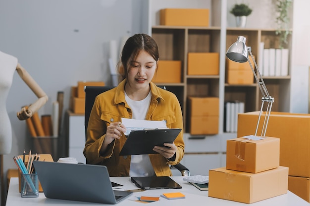 Mulheres de negócios de PME asiáticas usam computador portátil verificando encomendas de clientes em caixas de envio on-line em casa Começando empreendedor de pequenas empresas PME freelance Negócio on-line Trabalho em casa conceito