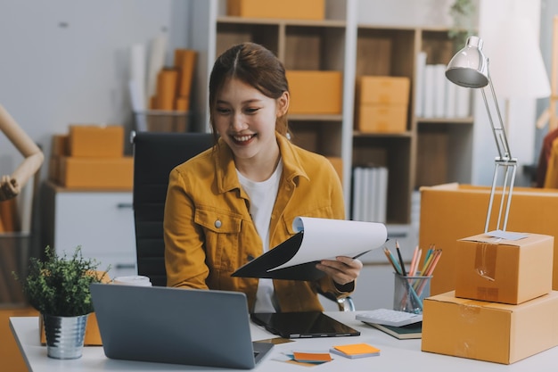 Mulheres de negócios de PME asiáticas usam computador portátil verificando encomendas de clientes em caixas de envio on-line em casa Começando empreendedor de pequenas empresas PME freelance Negócio on-line Trabalho em casa conceito