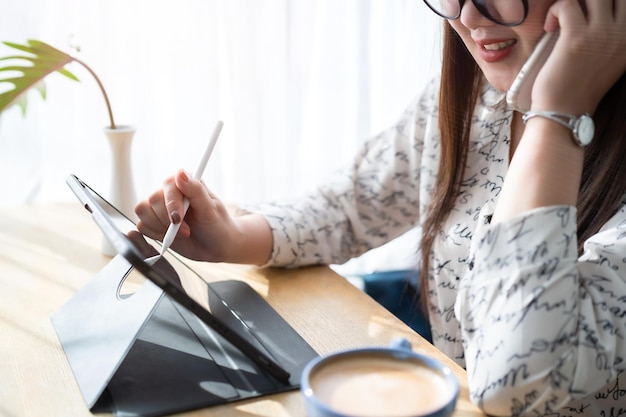 Mulheres de negócios freelance asiáticas conversando usando smartphone trabalhando com anotações em tablet digital com caneta eletrônica para navegar na internet conversando e blogando com uma xícara de café