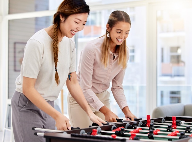 Mulheres de negócios jogando futebol de mesa rindo e se divertindo no escritório em seu trabalho corporativo Diversas colegas se unindo enquanto competiam em um jogo amigável de pebolim durante um intervalo juntos