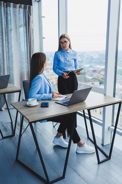 Mulheres de negócios ocupadas com um laptop no escritório assistindo conteúdo no laptop e discutindo o projeto juntos sentados no escritório durante uma pausa de trabalho Discussão corporativa de trabalho em equipe