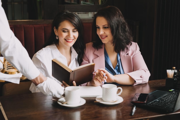 Mulheres de negócios sentam-se em um café bebem café e conversam sobre negócios, discutem negócios e se divertem