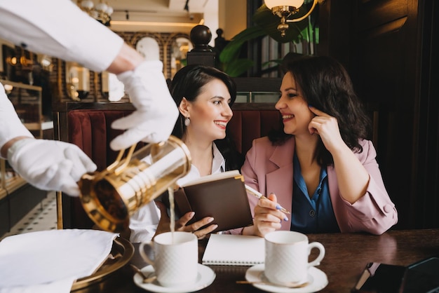 Mulheres de negócios sentam-se em um café bebem café e conversam sobre negócios, discutem negócios e se divertem