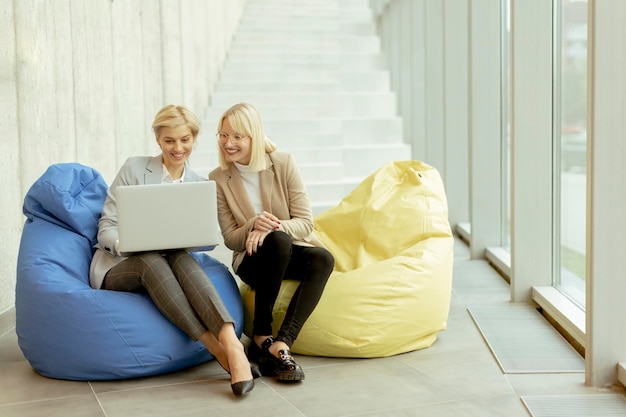 Mulheres de negócios usando laptop em sacos preguiçosos no escritório moderno