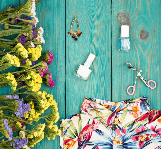 Mulheres de verão com vestido flores coloridas cosméticos maquiagem bijou e fundamentos em fundo azul de madeira