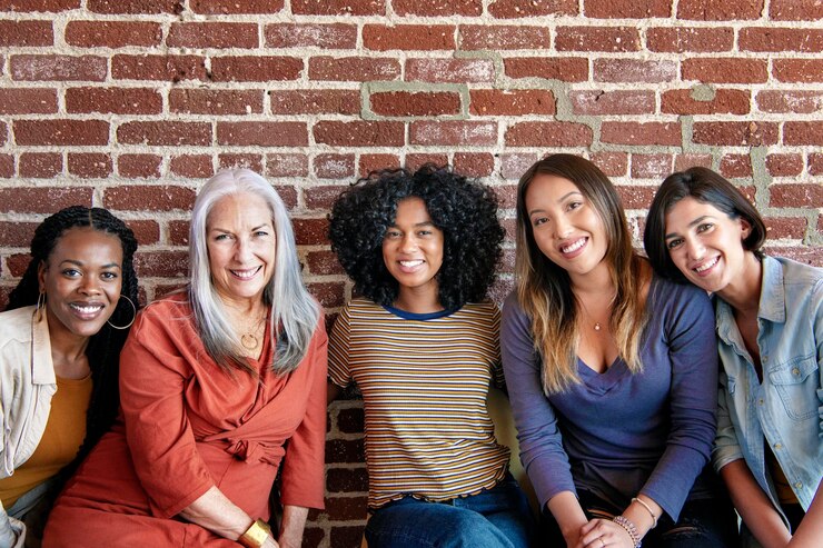 Foto mulheres diversas sentadas juntas junto a uma parede de tijolos