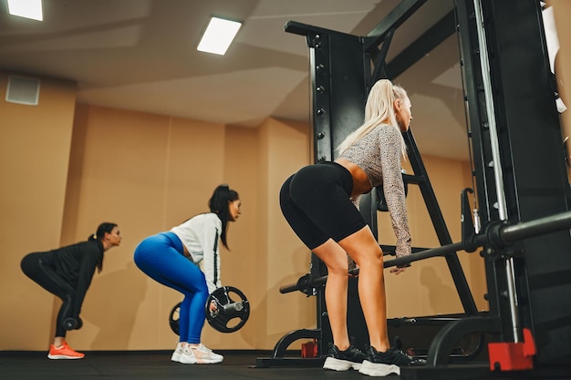 Mulheres do esporte de costas para a câmera realizando atividade de treinamento de levantamento terra com barra na academia