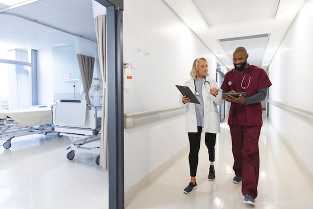 Mulheres e homens médicos felizes e diversos usando tablets, falando e andando no corredor do hospital