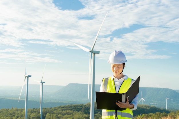 Mulheres engenheiras trabalhando e segurando o relatório na estação geradora de energia da fazenda de turbinas eólicas na montanhaTailândia