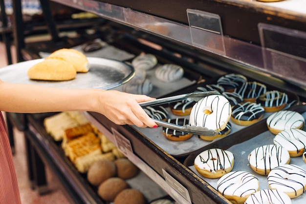 Mulheres escolhendo donut no supermercado. pinças para pães e bandeja.