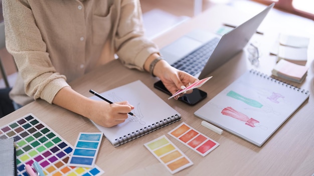 Mulheres estilistas escolhem amostras de cores para esboçar em papel para uma nova coleção criativa