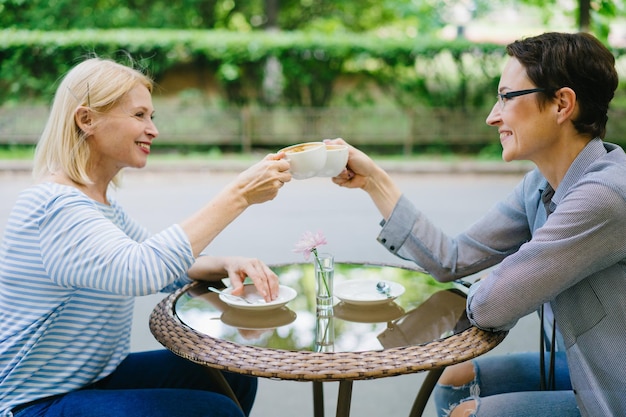 Mulheres felizes amigas tinindo xícaras de café no café ao ar livre aproveitando o dia de verão