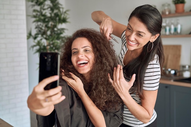 Mulheres felizes tirando selfie engraçado enquanto cortam o cabelo