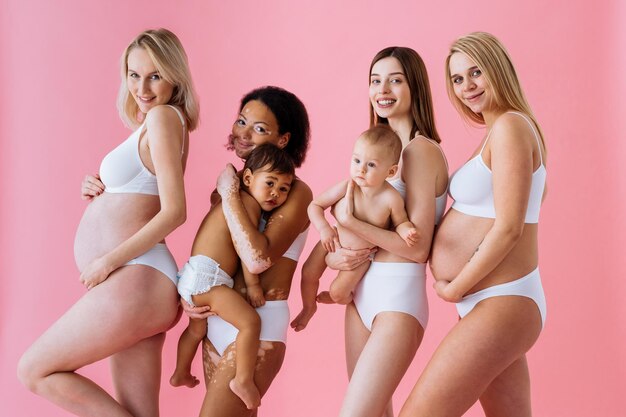 Mulheres grávidas felizes com barriga grande e lindas mães com bebês em estúdio