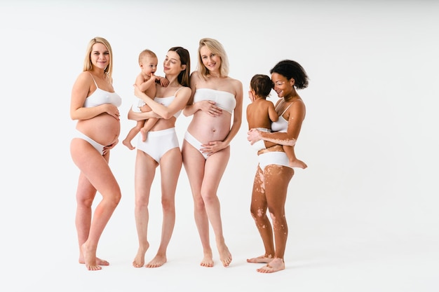 Mulheres grávidas felizes com barriga grande e lindas mães com bebês em estúdio