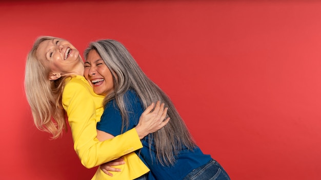 Mulheres idosas abraçando e rindo contra um fundo vermelho