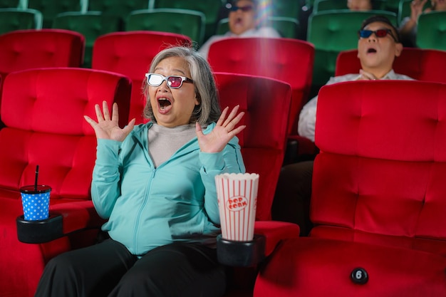 Mulheres idosas asiáticas com óculos assistem ansiosamente a filmes em 3D pipoca na mão saboreando
