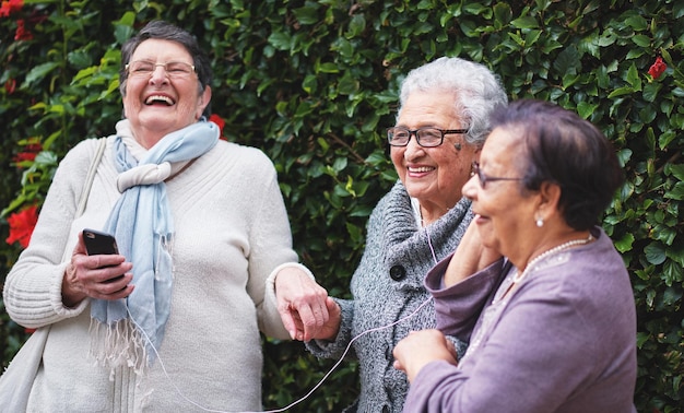 Mulheres idosas engraçadas ouvindo música no smartphone usando fones de ouvido sorrindo se divertindo comemorando a aposentadoria juntos ao ar livre