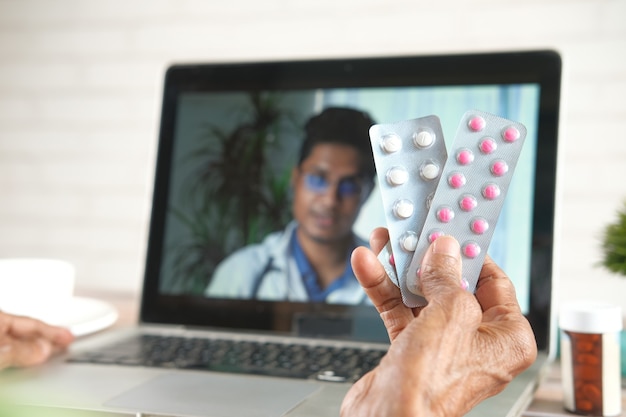 Mulheres idosas segurando blister durante a consulta com o médico no laptop