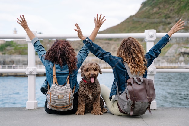 Foto mulheres irreconhecíveis com cachorro-d'água marrom. visão horizontal de mulheres viajando com animal de estimação. estilo de vida com animais ao ar livre.