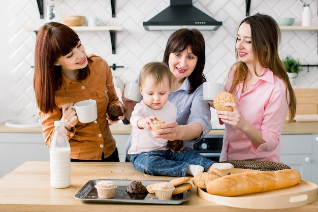 Mulheres jovens atraentes, mulher de meia idade e filha bonita estão cozinhando na cozinha. família amorosa, comendo seus muffins na cozinha e tomando café