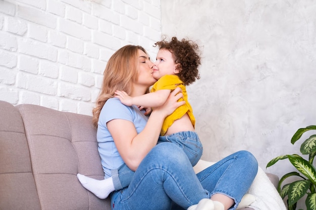 Mulheres jovens brincam com sua filha criança encaracolada no sofá, elas riem, abraçam e se divertem juntas