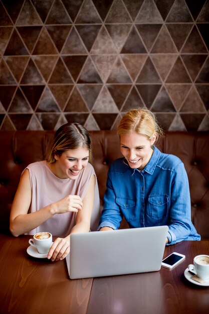 Mulheres jovens, com, laptop, sentando, pela tabela, em, café