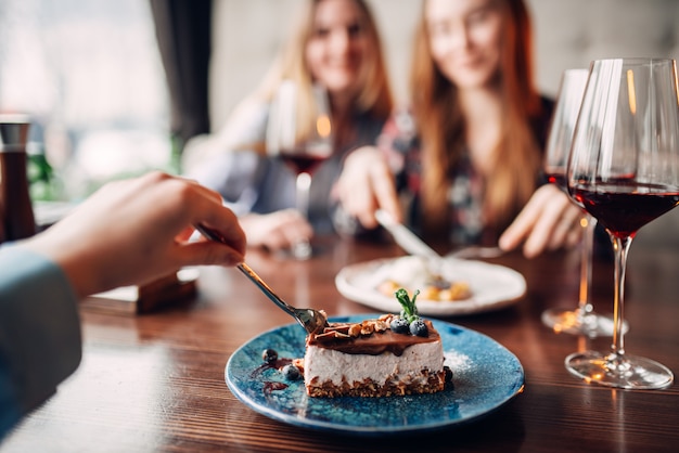 Mulheres jovens comem bolos doces no restaurante. Sobremesa de chocolate e álcool na mesa